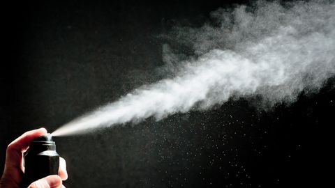 Vor schwarzem Hintergrund schiept ein Strahl Spray aus einer Deodorant-Sprühdose