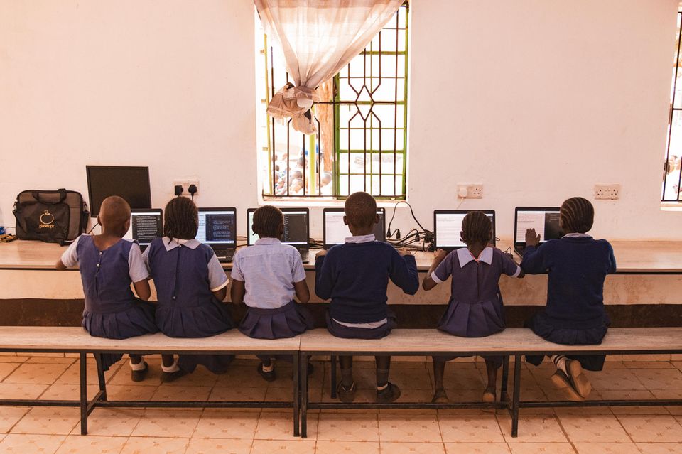 Schülerinnen und Schüler vor den neuen Laptops im Computerraum der Schule