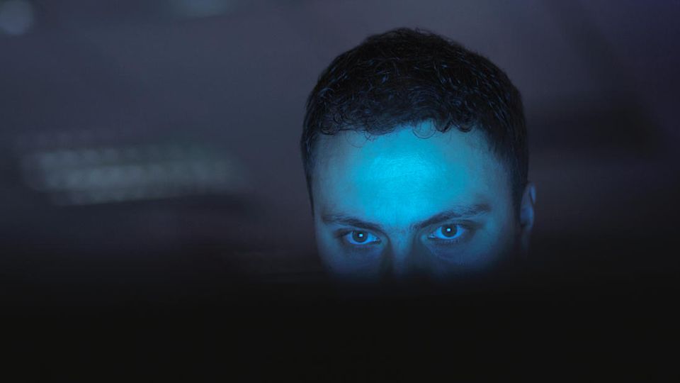 Ein nur halb sichtbarer Hacker sitzt vor einem Monitor