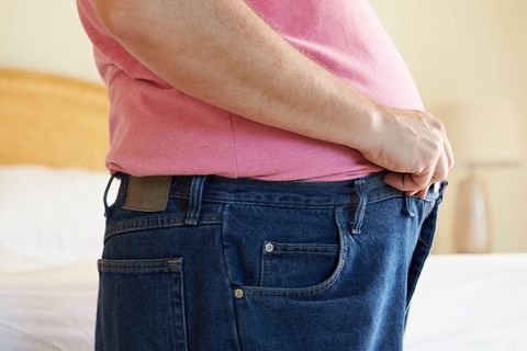 Mann versucht seine zu enge Hose zu schließen