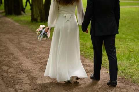 Ein Brautpaar geht Hand in Hand einen Feldweg entlang