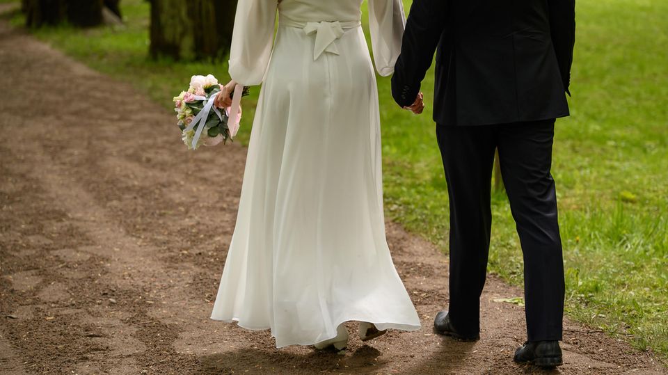 Ein Brautpaar geht Hand in Hand einen Feldweg entlang