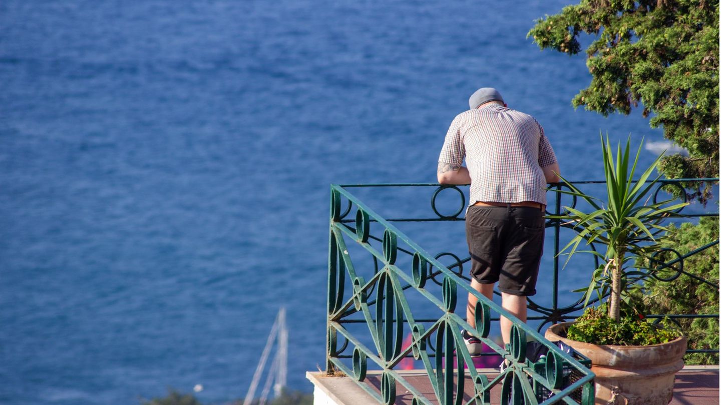 Ein Mann steht auf einem Balkon und schaut aufs Meer in Griechenland