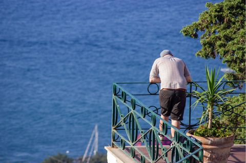 Ein Mann steht auf einem Balkon und schaut aufs Meer in Griechenland