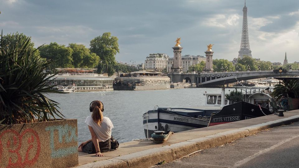 Frau sitzt an Fluss mit Blick auf Eiffelturm Frau sitzt an Fluss mit Blick auf Eiffelturm