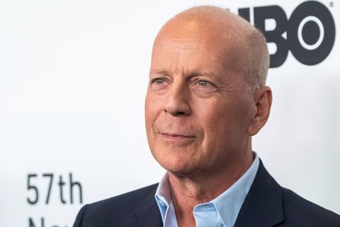 Bruce Wille, ein Mann mit Glatze und im Hemd, steht vor einer Wand