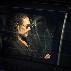 Russell Brand sitzt mit Sonnenbrille in einem dunklen Auto
