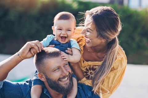 Ein Baby sitzt auf den Schultern seine Vaters und Vater, Mutter und Kind lachen