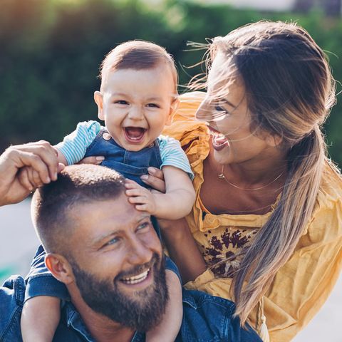 Ein Baby sitzt auf den Schultern seine Vaters und Vater, Mutter und Kind lachen