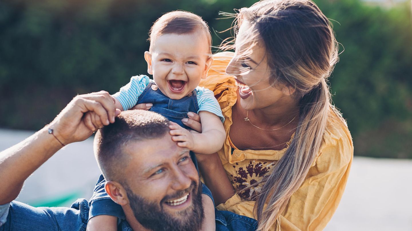 Ein Baby sitzt auf den Schultern seine Vaters und Vater, Mutter und Kind lachen