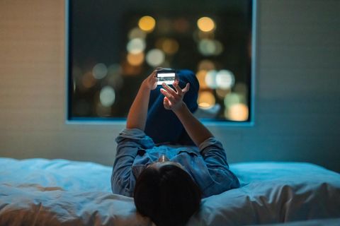 Eine Jugendliche liegt auf dem Rücken im Bett und sieht Fotos auf ihrem Handy an