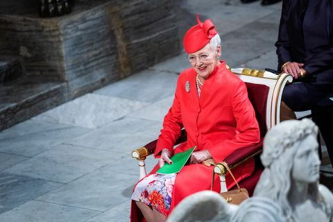 Königin Margarethe II. von Dänemark sitzt lächelnd in einem roten Kostüm auf einem Stuhl.