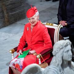 Königin Margarethe II. von Dänemark sitzt lächelnd in einem roten Kostüm auf einem Stuhl.