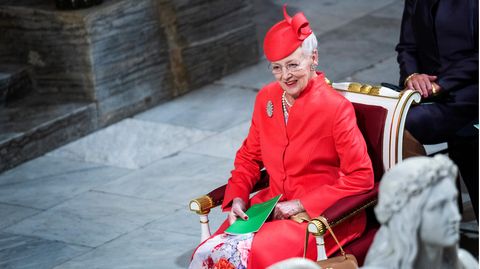 Königin Margarethe II. von Dänemark sitzt lächelnd in einem roten Kostüm auf einem Stuhl.