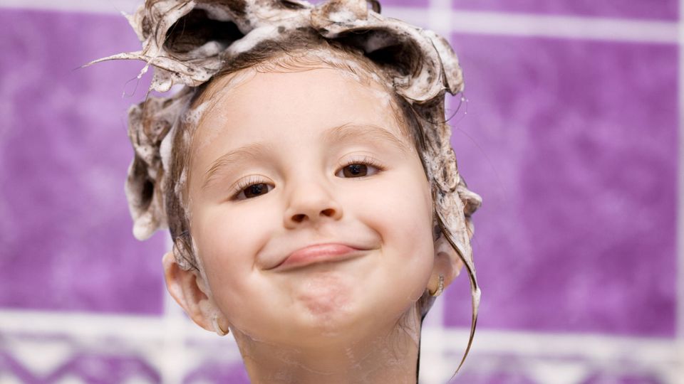 Kind mit Schaum im Haar grinst in der Badewanne