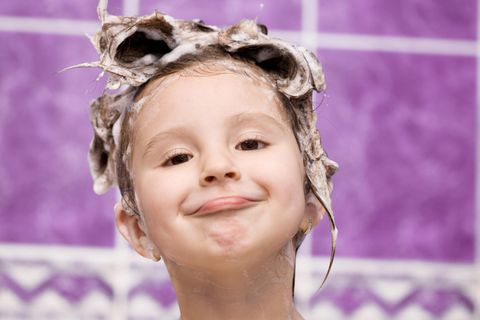 Kind mit Schaum im Haar grinst in der Badewanne
