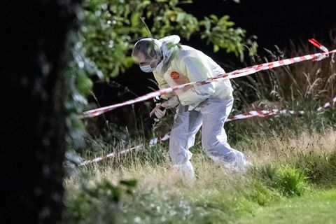Ein Mensch in weißem Overall und FFP2-Maske nähert sich einem ausgeleuchteten Fundort einer Frauenleiche in Hessen