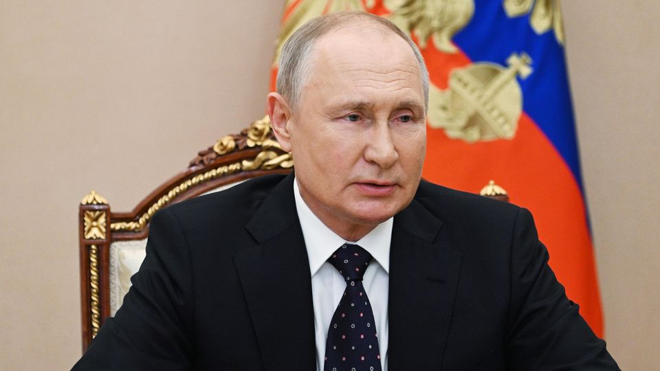 Wladimir Putin sitzt im Anzug und mit gefalteten Händen an einem Schreibtisch vor einer russischen Flagge
