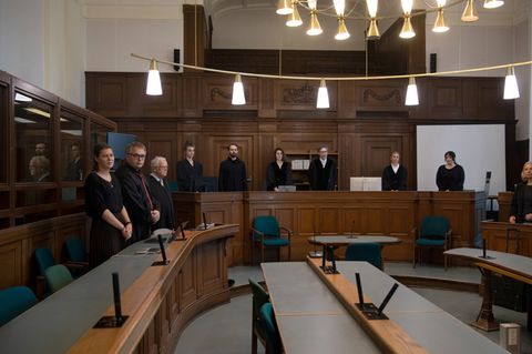 Foto in einen Gerichtssaal mit stehen Richtern und weiteren Personen