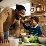 Ein Kind füttert seinen Papa mit einer Gabel, beide lachen