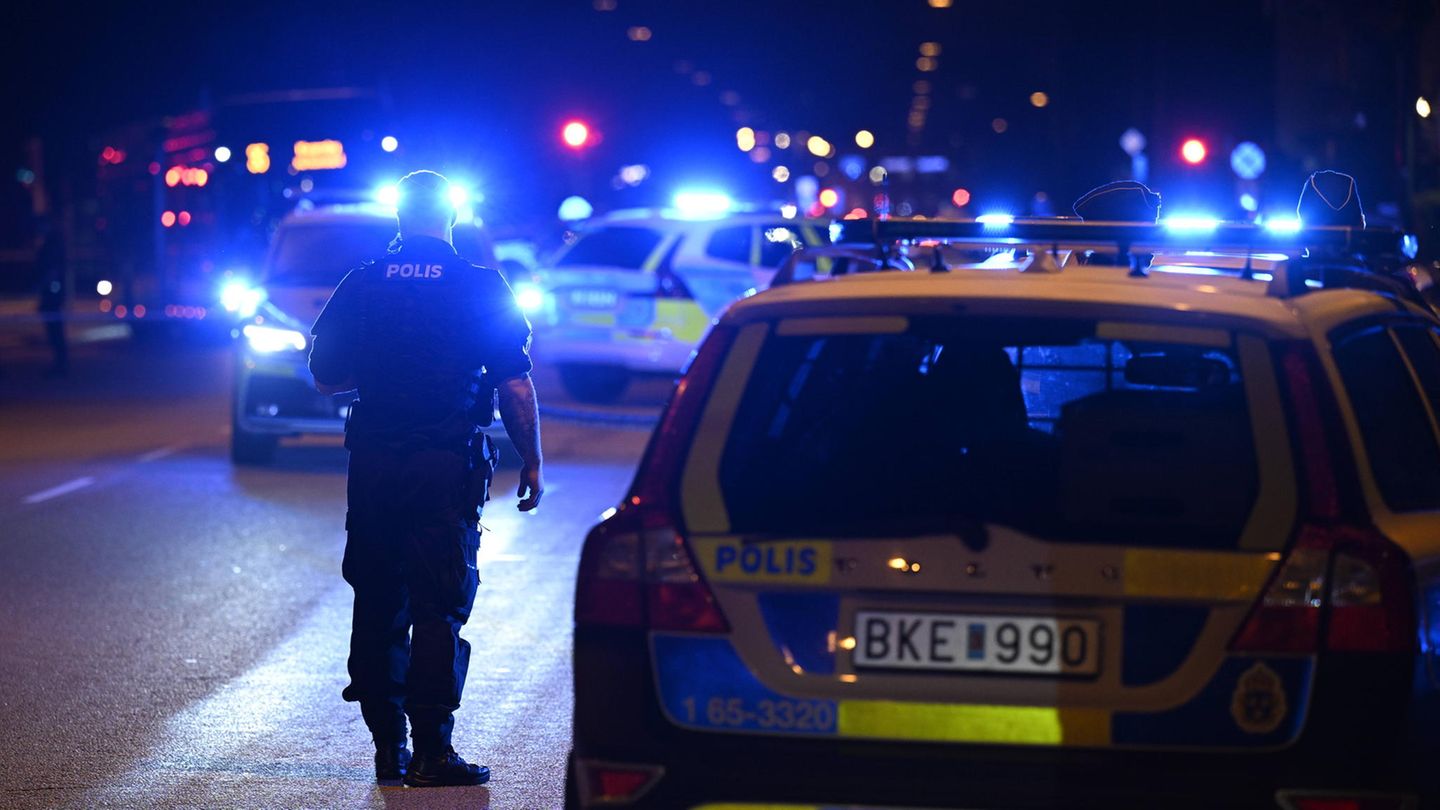 Ein Polizist steht in Schweden vor Polizeiwagen mit Blaulicht