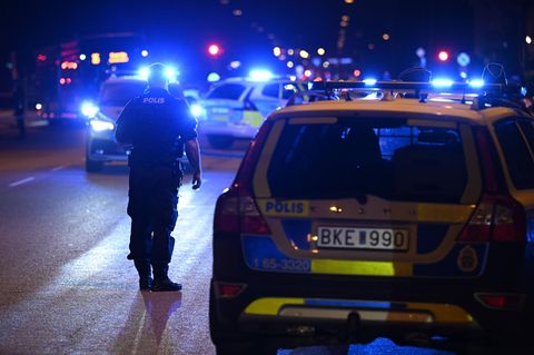 Ein Polizist steht in Schweden vor Polizeiwagen mit Blaulicht