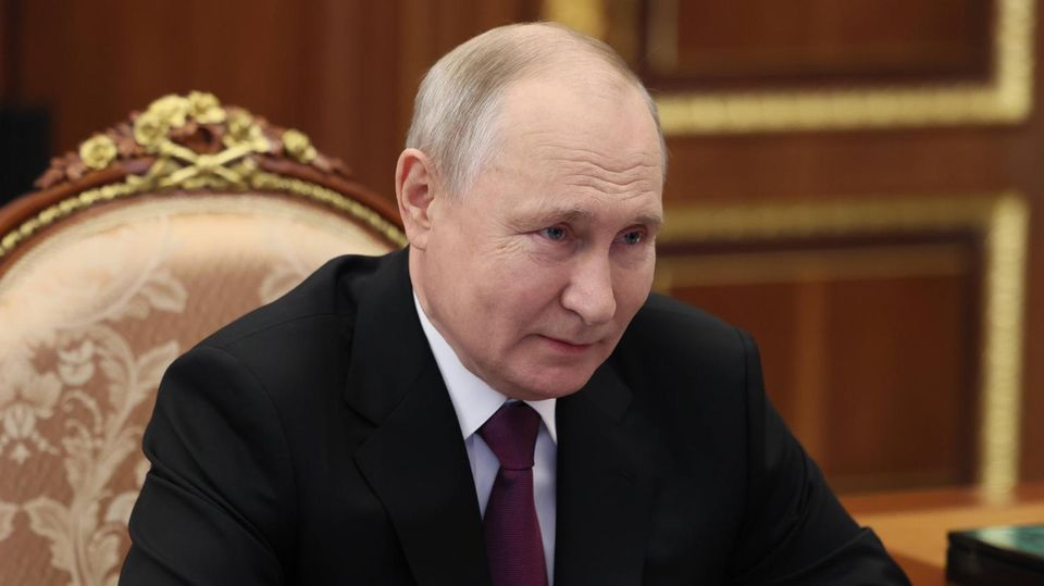 Wladimir Putin, ein Mann mit schütterem Haar, sitzt im Anzug auf einem thronähnlichen Stuhl