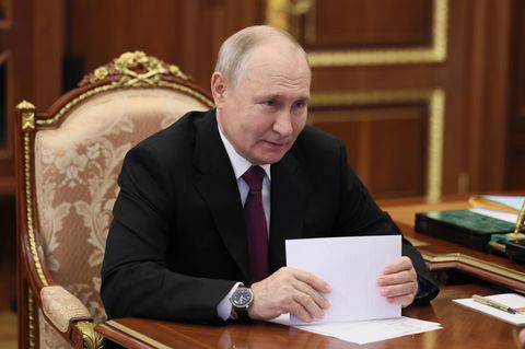 Wladimir Putin, ein Mann mit schütterem Haar, sitzt im Anzug auf einem thronähnlichen Stuhl