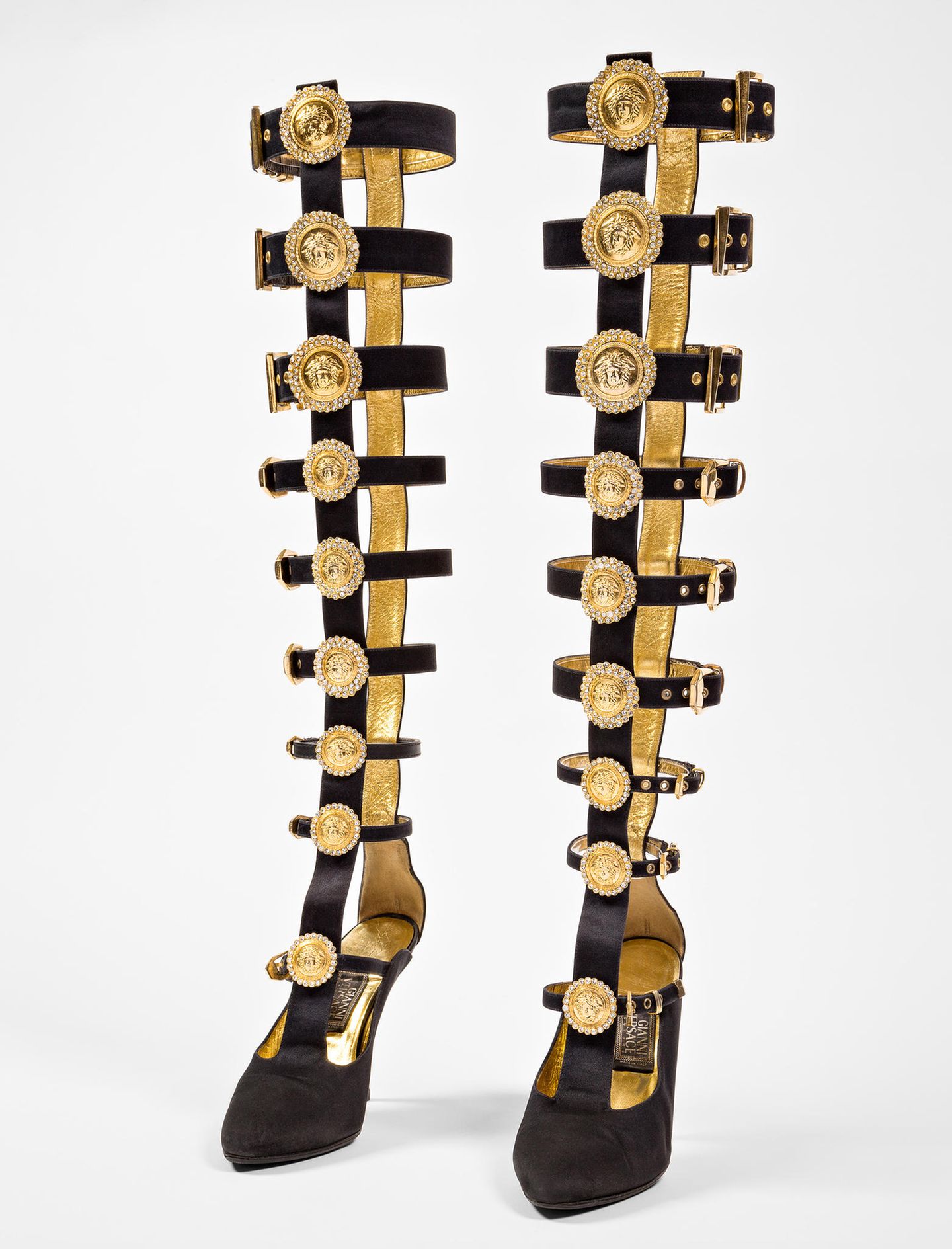 "Ein Aufeinandertreffen von Dschungel und Hofstaat", so beschrieb einmal die "New York Times" die Designs von Gianni Versace: leuchtende Farben einerseits und tiefes Schwarz andererseits, Riemen, Schnallen, metallische Akzente, der goldene Medusenkopf in seinem Logo sind Teil seiner Markenästhetik.   Gold, Riemen, Medusaköpfe – das Modell aus dem Jahr 1992 vereint alle Elemente, die für den Versace-Still so kennzeichnend sind.   Gianni Versace designte bis zu seinem gewaltsamen Tod im Jahr 1997. Dann übernahm seine Schwester Donatella die Leitung des Labels. Sie hatte bereits häufig mit ihrem Bruder zusammengearbeitet und präsentierte nur zwölf Wochen nach dessen Tod ihre erste Kollektion. Für ihren eigenen Stil griff sie Aspekte seiner Designphilosophie auf und entwickelte die Versace-Ästhetik weiter. "Manche meinten, Giannis Mode sei vulgär ... aber Frauen lieben sie nun mal, nicht weil sie Haut zeigte, sondern weil er die Frauen stark machte. Er sagte ihnen, sie sollten keine Angst vor ihrer Sexualität haben", erklärte Donatella. 