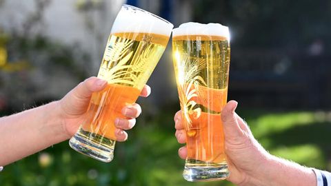 Mit Bier gefüllte Gläser, mit denen zwei Personen anstoßen