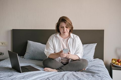 Junge Frau sitzt auf Bett und schaut auf Handy. Auf Tiktok wird viel über psychische Krankheiten gesprochen