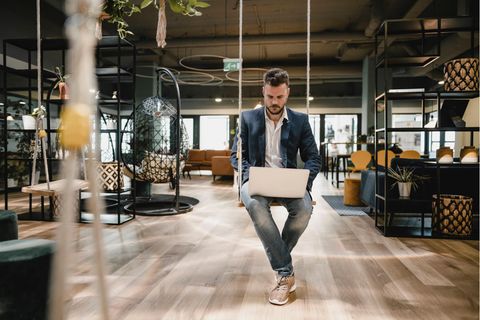 Ein Mann sitzt mit einem Laptop auf einer Schaukel in einem Büro