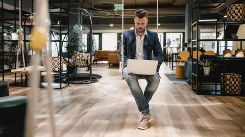 Ein Mann sitzt mit einem Laptop auf einer Schaukel in einem Büro