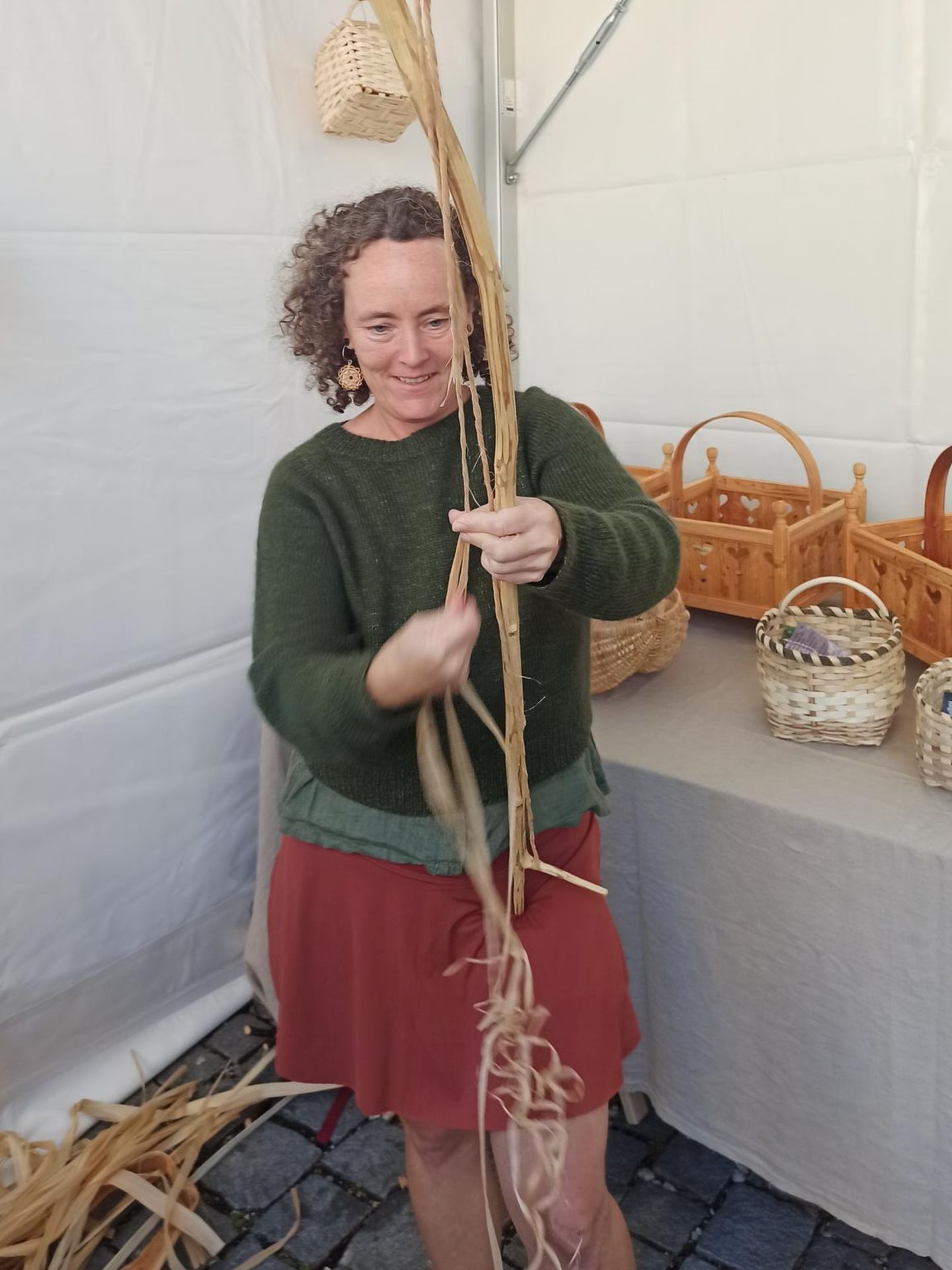 Frau mit grünem Pullover hält eine Stange mit Baststreifen