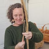 Frau mit grünem Pullover hält eine Stange mit Baststreifen