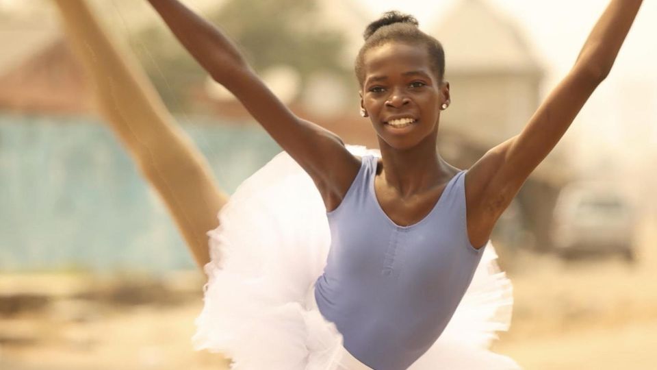 schwarzes Mädchen in einem Ballet-Tutu in tanzender Pose, im Hintegrund Slums Afrikas