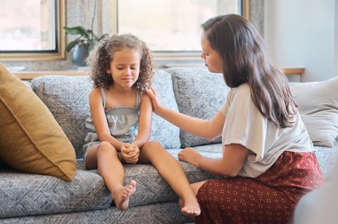 Ein Mädchen sitzt auf einem Sofa und wird von der Mutter getröstet