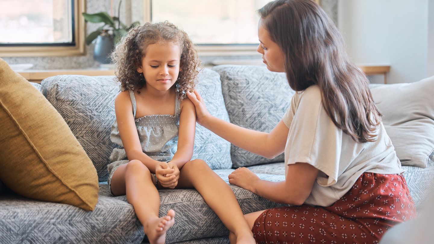 Ein Mädchen sitzt auf einem Sofa und wird von der Mutter getröstet