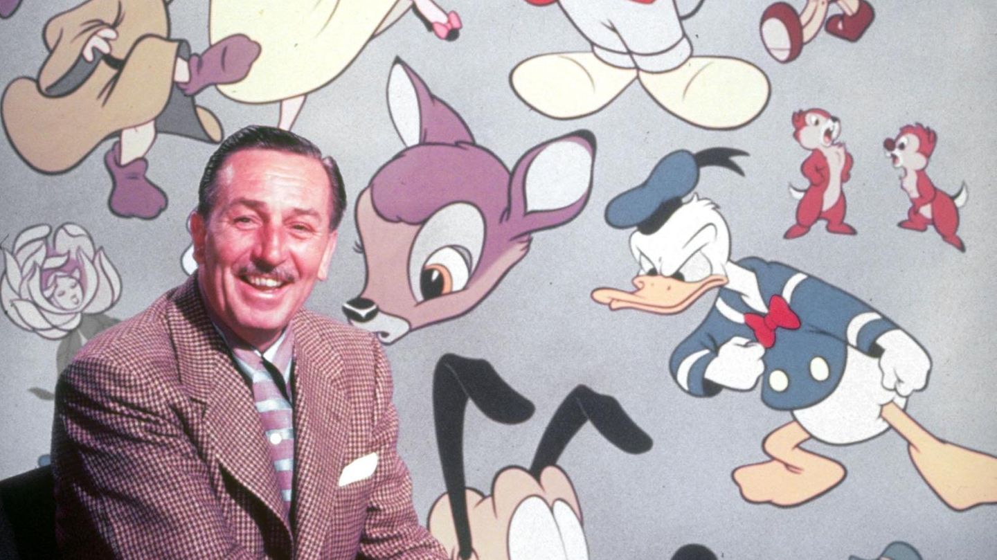 Walt Disney sitzt vor einer Wand mit den berühmtesten Disney-Figuren Walt Disney sitzt vor einer Wand mit den berühmtesten Disney-Figuren