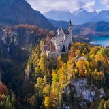 Blick auf Schloss Neuschwantsein – eingebettet in die Herbslandschaft vor Bäumen und Bergen