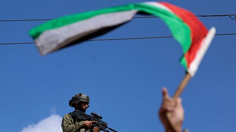 Ein Mann schwenkt eine palästinensische Flagge, während ein israelischer Soldat bei Zusammenstößen zusieht
