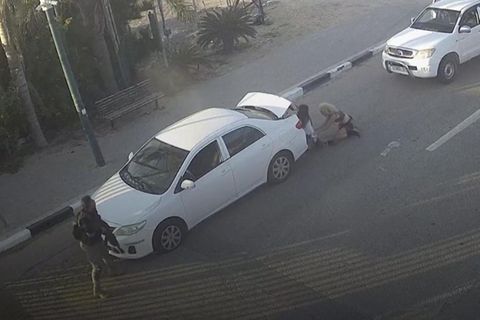 Zwei Frauen verstecken sich hinter Auto, links israelischer Polizist