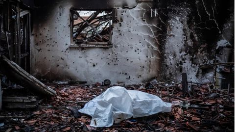 In einem zerstörten Haus liegt eine Leiche unter weißem Tuch.