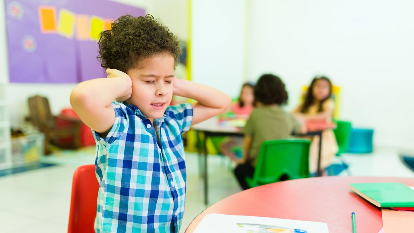 Ein Junge hält sich im Klassenzimmer die Ohren zu