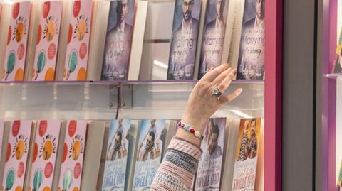 Frau greift nach einem Buch in einem Regal