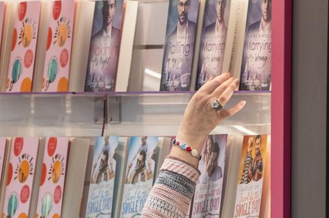 Frau greift nach einem Buch in einem Regal