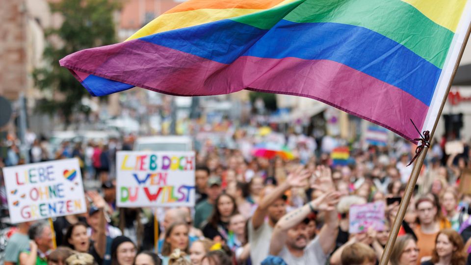 Eine Menschenmenge am CSD: Jemand schwenkt eine große Regenbogenfahne