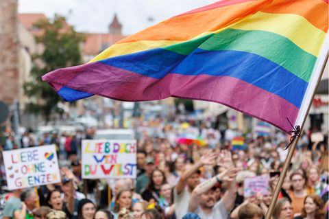 Eine Menschenmenge am CSD: Jemand schwenkt eine große Regenbogenfahne