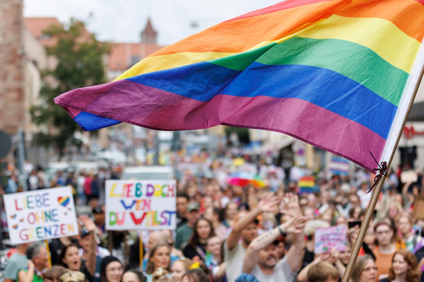 Eine Menschenmenge am CSD: Jemand schwenkt eine große Regenbogenfahne