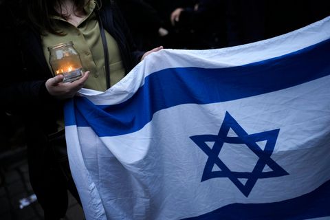 Eine Frau hält eine Kerze und eine israelische Flagge, während sie an einer Mahnwache vor einer Synagoge in Berlin, Deutschland, teilnimmt, Freitag, 13. Oktober 2023. Hunderte Berlinerinnen und Berliner versammelten sich am Vorabend des Schabbat vor der Synagoge am Fraenkelufer, um sie und den darin stattfindenden Gebetsgottesdienst vor möglichen Anschlägen zu schützen.